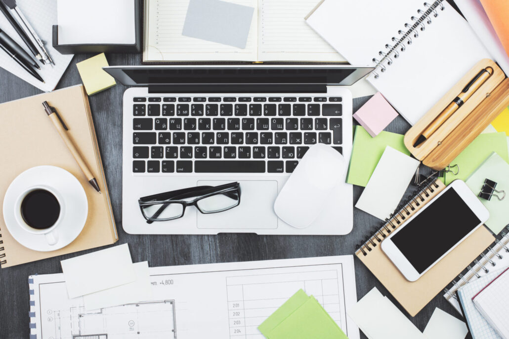 Mix of office supplies, laptop computer and mobile phone on contemporary wooden desk top with other items. Above view. Mock up