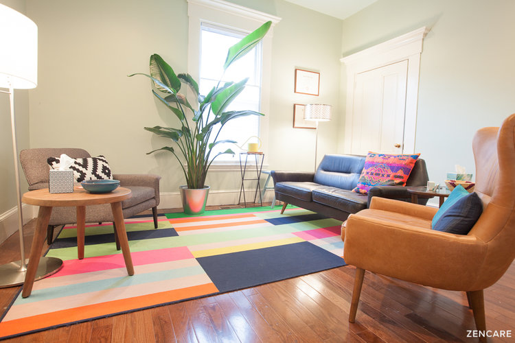 Office space with a colorful rug and large plant next to a chair and couch